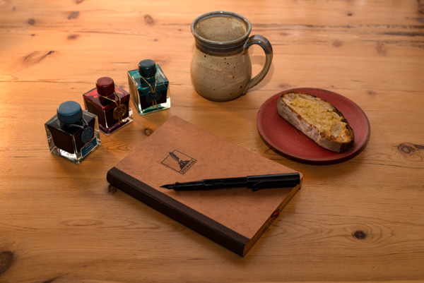 Journal, ink, fountain pen and snack on desk